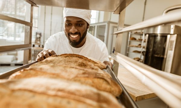 26163851-smiling-african-american-baker-looking-at-fresh-loaves-of